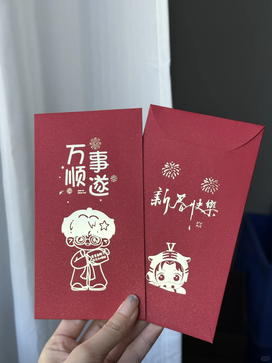 手持同款红包的正面与背面，闭合封口，烫印在此角度呈浅色反光。
